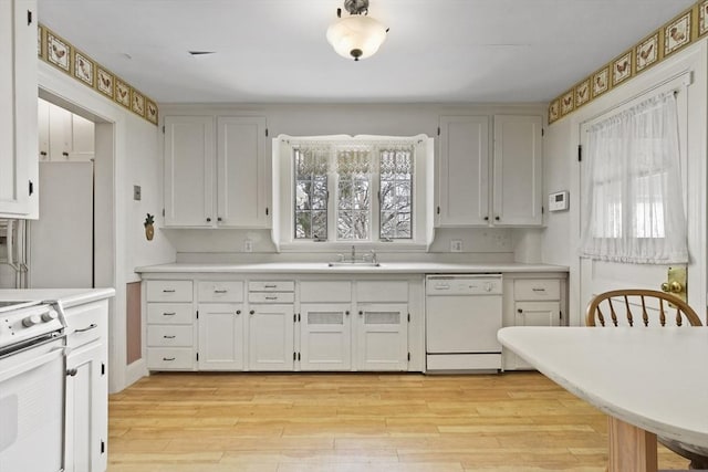 kitchen with white cabinets, white appliances, light hardwood / wood-style floors, and sink