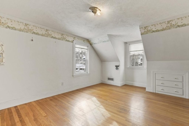 additional living space with light wood-type flooring, a textured ceiling, and vaulted ceiling