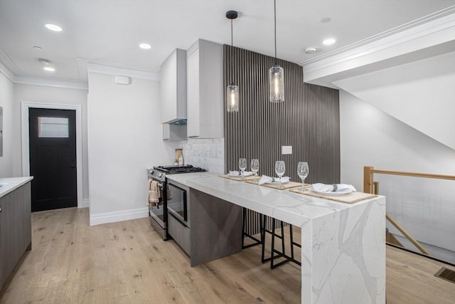 kitchen with pendant lighting, light hardwood / wood-style flooring, light stone counters, and stainless steel range with gas stovetop