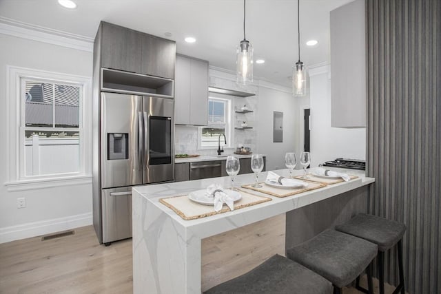 kitchen featuring kitchen peninsula, appliances with stainless steel finishes, light wood-type flooring, a kitchen breakfast bar, and pendant lighting