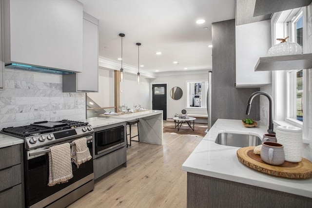 kitchen featuring light wood-type flooring, tasteful backsplash, stainless steel gas range, sink, and pendant lighting