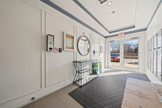 corridor with a raised ceiling, french doors, and ornamental molding