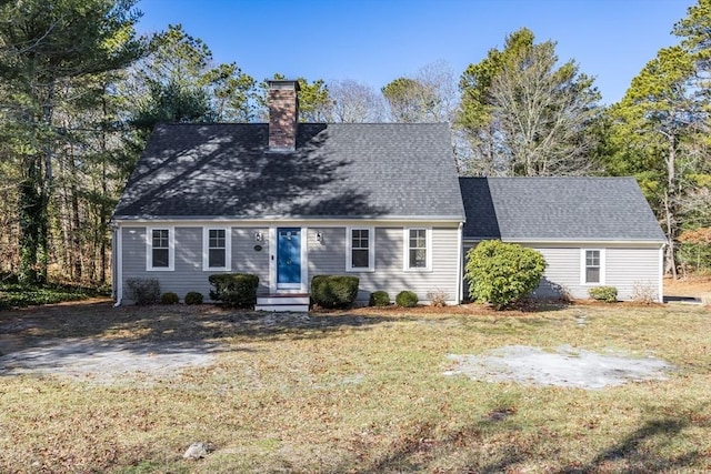 new england style home with entry steps, roof with shingles, a chimney, and a front lawn