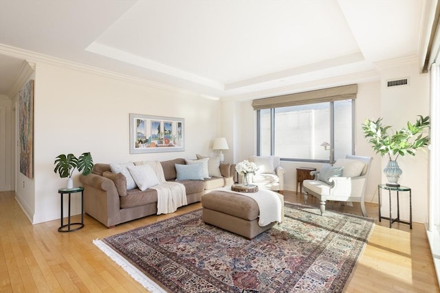 living room with light wood-type flooring, crown molding, and a tray ceiling