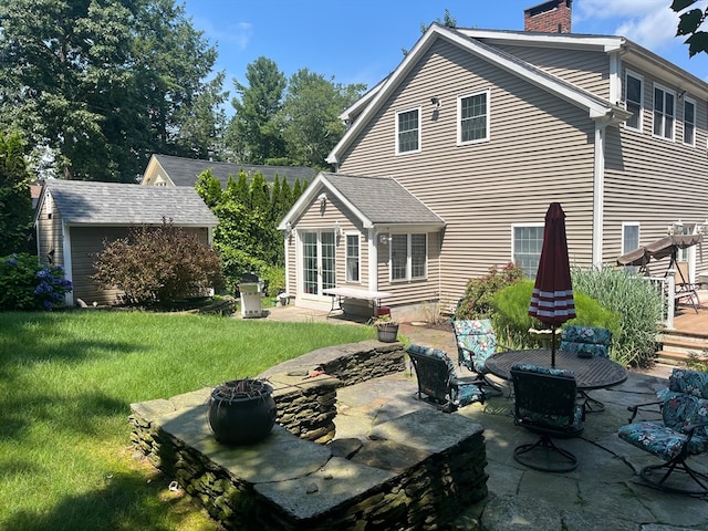 rear view of property featuring a patio, an outbuilding, a lawn, and a fire pit