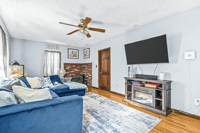 living room with ceiling fan, wood-type flooring, and a brick fireplace