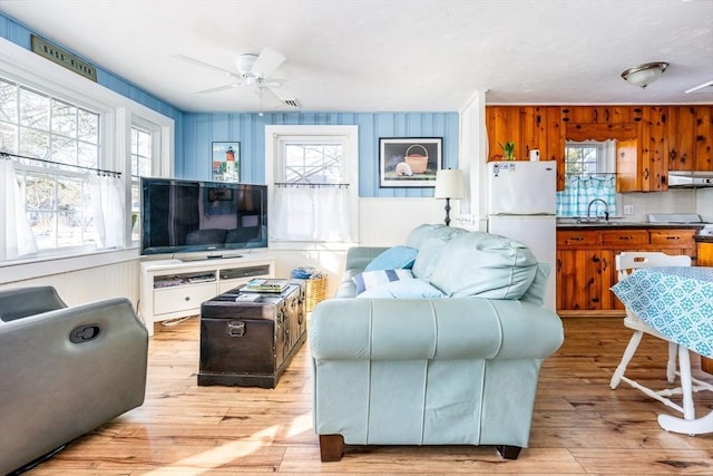 living room with ceiling fan, sink, wooden walls, and light wood-type flooring