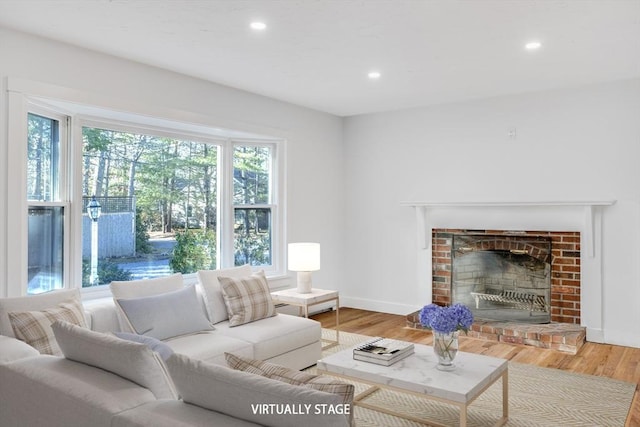 living area with recessed lighting, baseboards, a brick fireplace, and wood finished floors