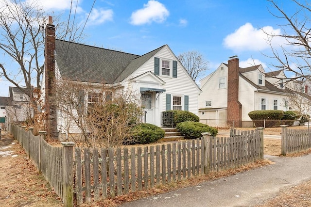 new england style home featuring a fenced front yard and a shingled roof