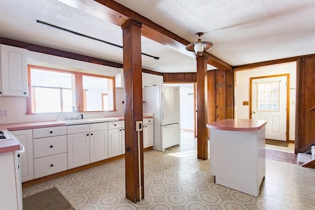 kitchen featuring a kitchen island, white cabinetry, sink, white refrigerator, and beam ceiling