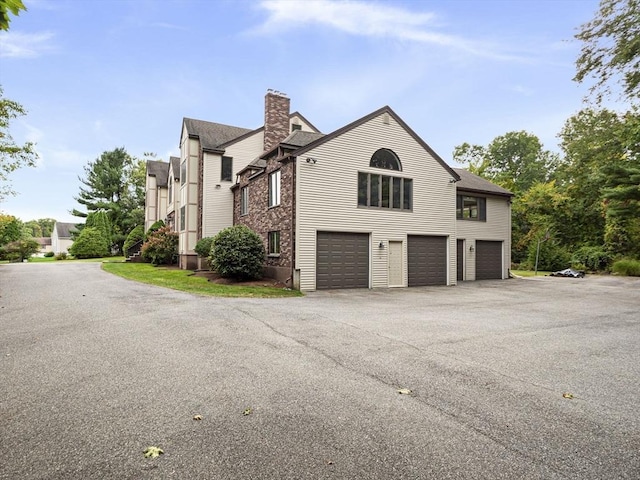 view of property exterior with an attached garage, a chimney, and aphalt driveway