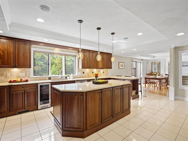 kitchen with hanging light fixtures, wine cooler, a kitchen island, and a raised ceiling