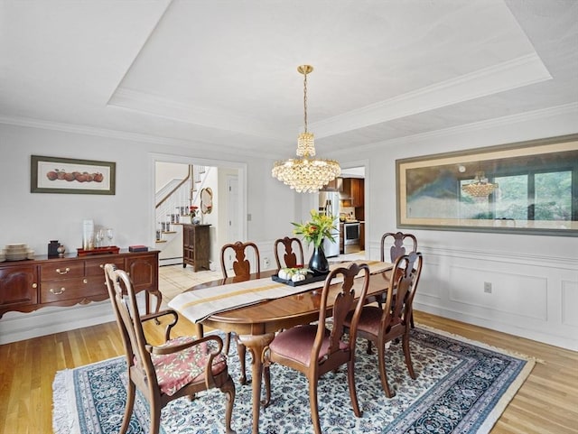 dining area with light wood-type flooring, a raised ceiling, and stairs