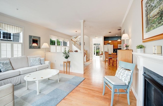 living room featuring light wood finished floors, a glass covered fireplace, stairs, and ornamental molding