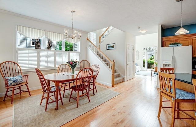 dining area with light wood-style floors, baseboards, stairs, and an inviting chandelier