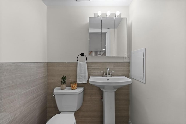 bathroom featuring toilet, tile walls, and sink