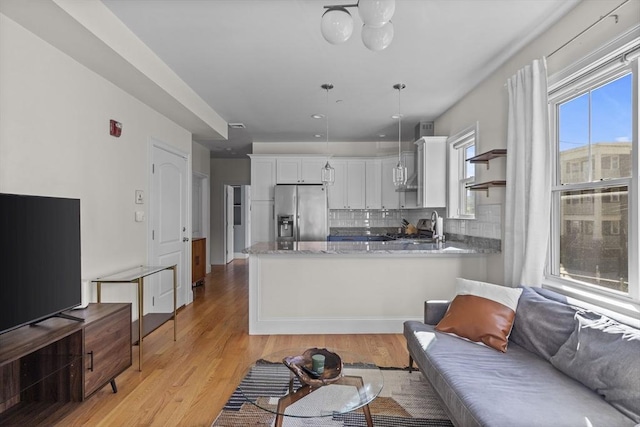 kitchen with kitchen peninsula, stainless steel fridge, backsplash, decorative light fixtures, and white cabinets