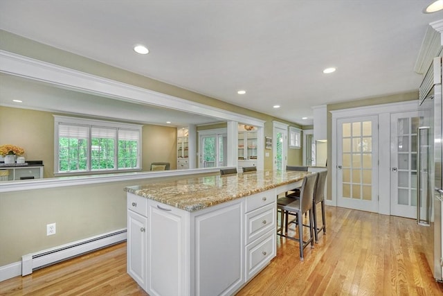 24 Cory Ln, Reading, MA 01867 - kitchen with a baseboard heating unit, white cabinetry, a kitchen breakfast bar, light wood-style flooring, and a center island