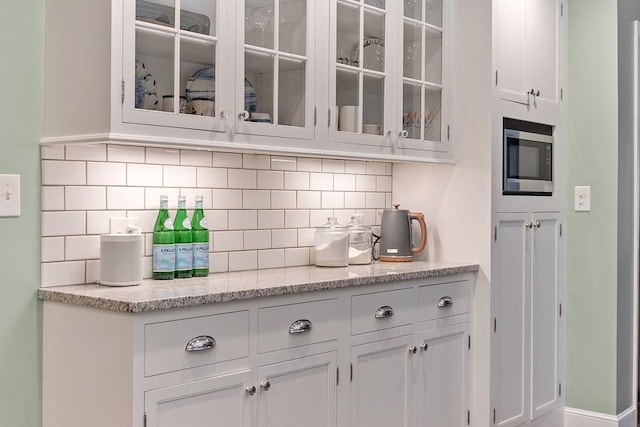 15 Saxon Ln, Shrewsbury, MA 01545 - kitchen featuring white cabinets, decorative backsplash, stainless steel microwave, glass insert cabinets, and light stone countertops