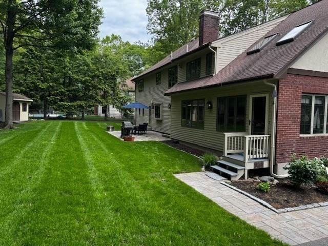 15 Saxon Ln, Shrewsbury, MA 01545 - rear view of house featuring a chimney, a yard, brick siding, a patio, and roof with shingles