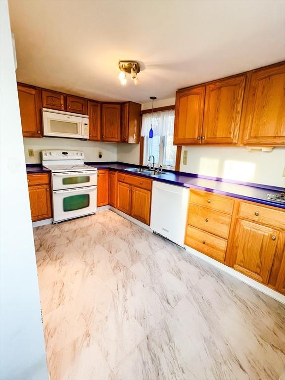 kitchen featuring brown cabinetry, dark countertops, white appliances, and a sink