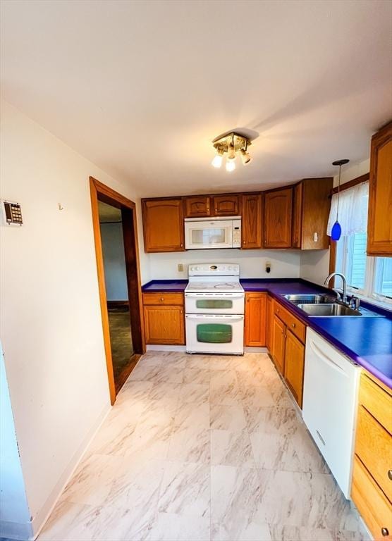 kitchen featuring marble finish floor, brown cabinets, dark countertops, a sink, and white appliances