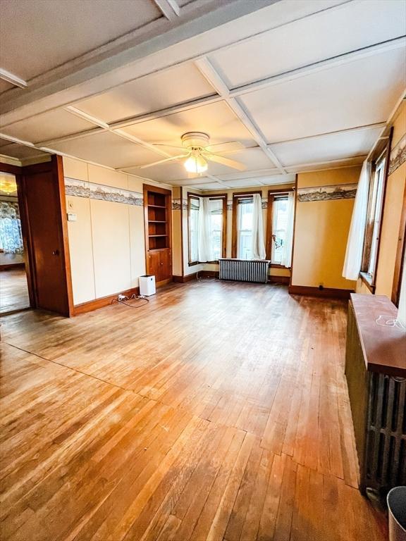 unfurnished living room featuring baseboards, coffered ceiling, radiator, ceiling fan, and light wood-style flooring