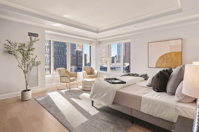 bedroom with wood finished floors, visible vents, baseboards, a view of city, and a tray ceiling