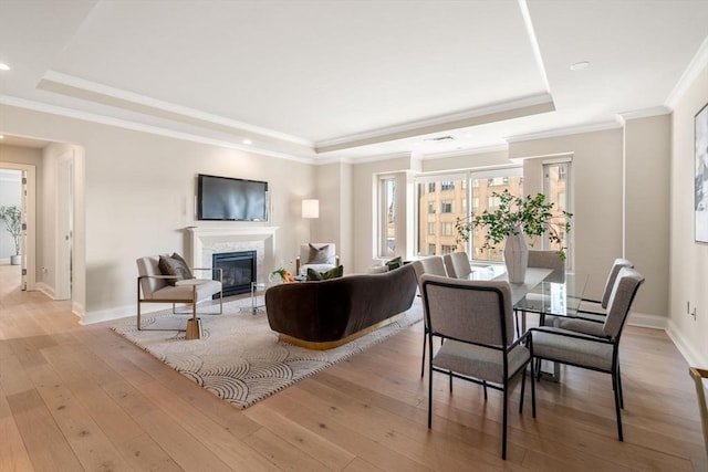 living area featuring light wood-type flooring, a tray ceiling, and a tiled fireplace