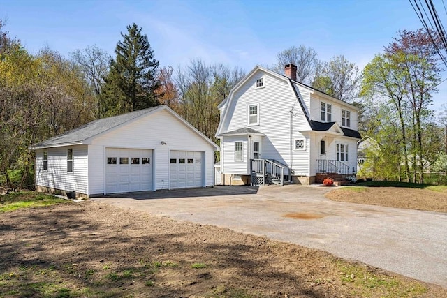 view of side of home featuring a gambrel roof, a chimney, an outdoor structure, and a garage