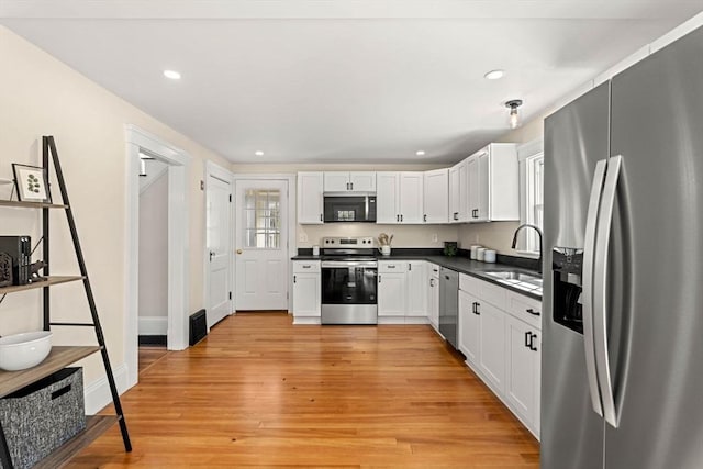 kitchen featuring white cabinets, dark countertops, appliances with stainless steel finishes, a sink, and light wood-style floors