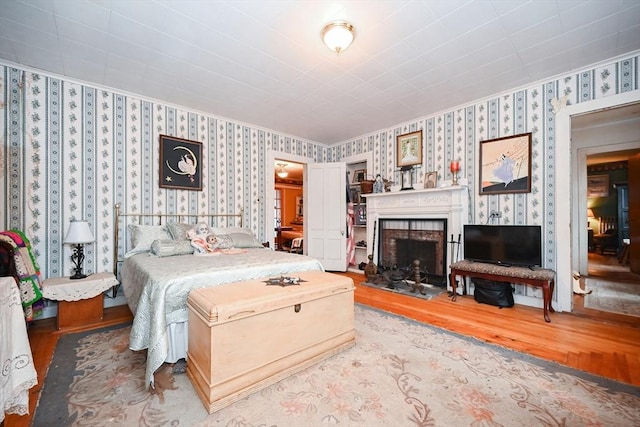 bedroom featuring a fireplace, wood-type flooring, and crown molding