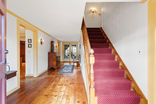 stairs featuring french doors, crown molding, baseboards, and hardwood / wood-style floors