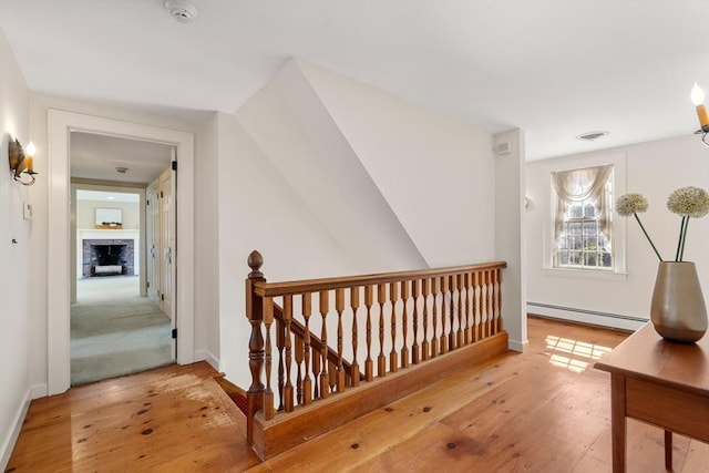 hallway with visible vents, baseboards, a baseboard radiator, an upstairs landing, and wood-type flooring