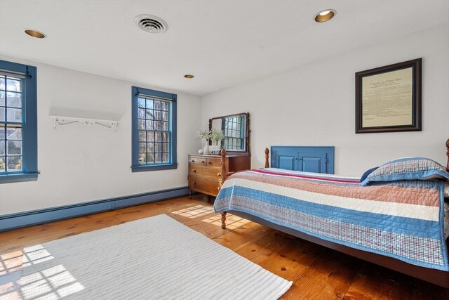 bedroom featuring wood finished floors, visible vents, multiple windows, and a baseboard heating unit