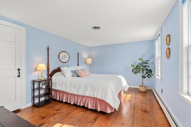 bedroom with hardwood / wood-style floors, baseboards, visible vents, and a baseboard radiator