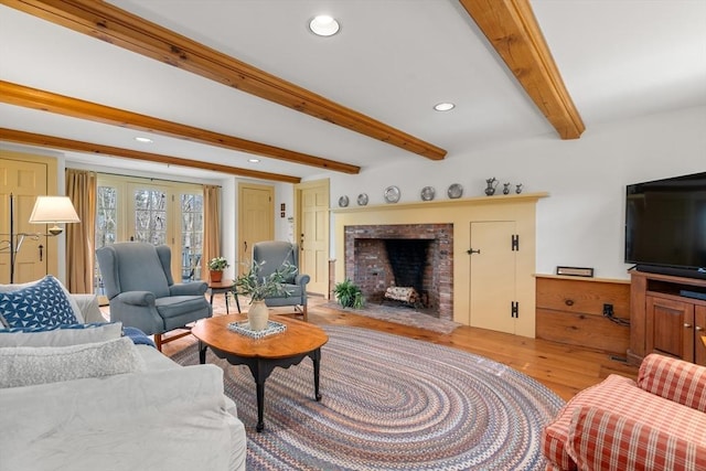 living room with a brick fireplace, recessed lighting, light wood-style floors, and beamed ceiling