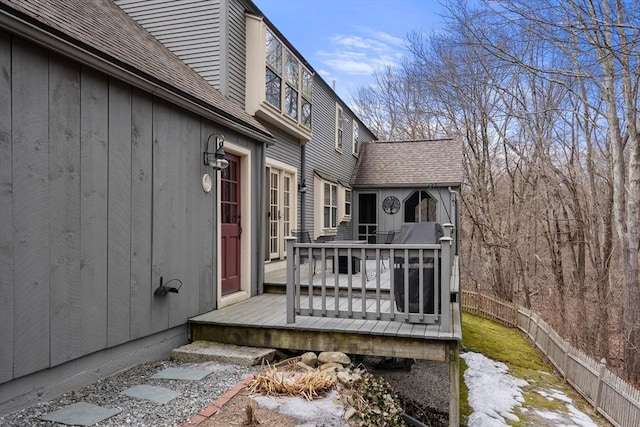 view of home's exterior with a wooden deck, fence, and a shingled roof