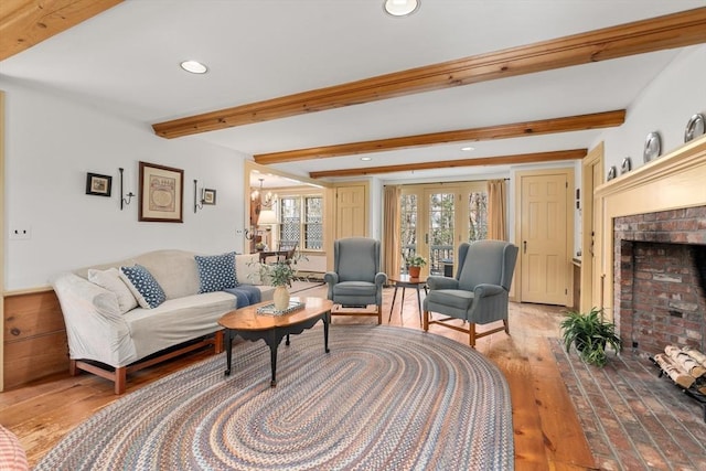 living room with a brick fireplace, beamed ceiling, light wood-type flooring, recessed lighting, and an inviting chandelier