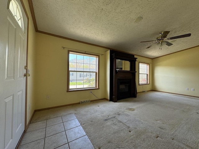 unfurnished living room featuring visible vents, crown molding, a glass covered fireplace, baseboards, and carpet