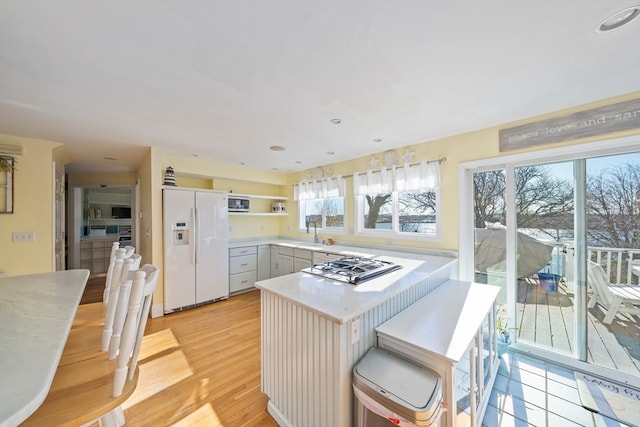 kitchen featuring a kitchen bar, light hardwood / wood-style floors, stainless steel gas stovetop, sink, and white fridge with ice dispenser