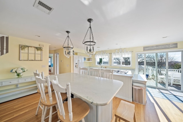 kitchen with a kitchen island, light wood-type flooring, white cabinetry, white fridge with ice dispenser, and pendant lighting