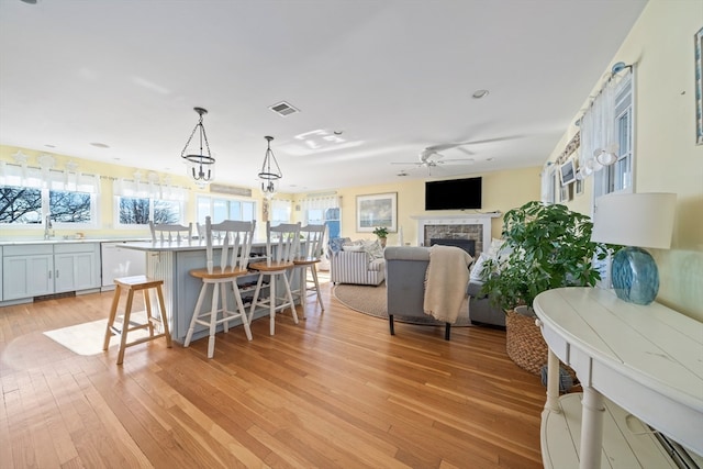 kitchen with a breakfast bar area, a kitchen island, pendant lighting, a fireplace, and light hardwood / wood-style flooring