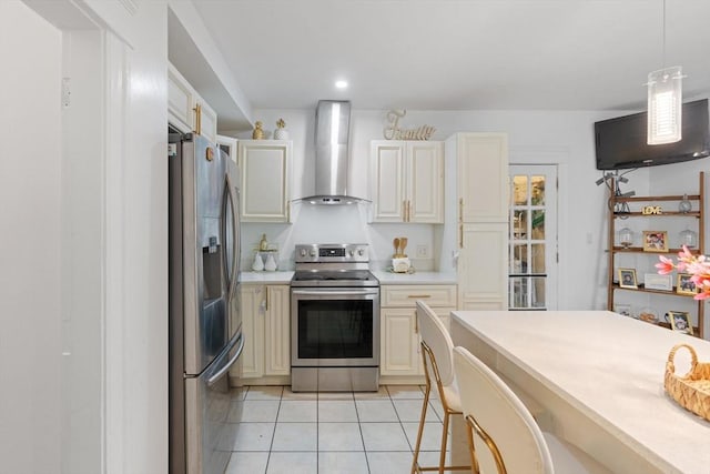 kitchen featuring light tile patterned flooring, wall chimney range hood, hanging light fixtures, and appliances with stainless steel finishes