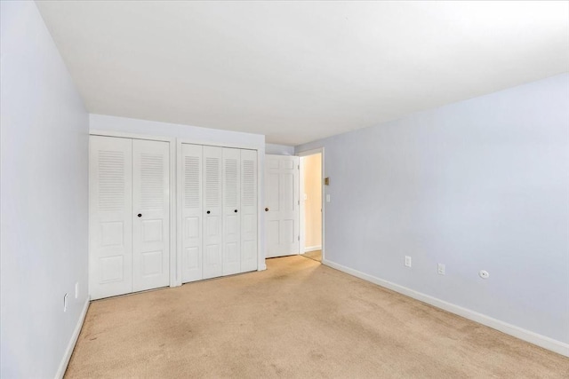 unfurnished bedroom featuring two closets and light carpet