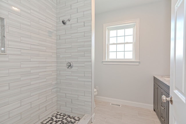 bathroom with vanity, toilet, a tile shower, and tile patterned flooring