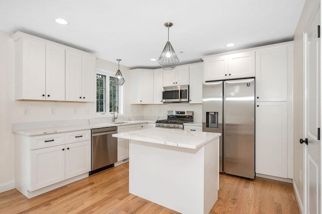 kitchen featuring light wood-type flooring, appliances with stainless steel finishes, decorative light fixtures, a kitchen island, and white cabinetry