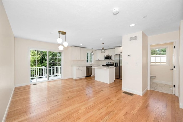 kitchen with appliances with stainless steel finishes, pendant lighting, white cabinetry, light hardwood / wood-style flooring, and a kitchen island