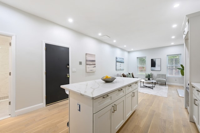 kitchen featuring white cabinetry, light hardwood / wood-style flooring, light stone counters, and a kitchen island