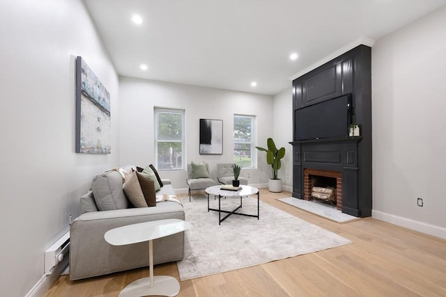 living room featuring a baseboard radiator, light hardwood / wood-style floors, and a large fireplace